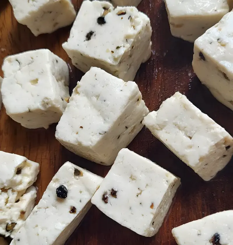 Cubes of PANEVO Black Pepper paneer on a dark wooden board, cracked peppercorns visible inside