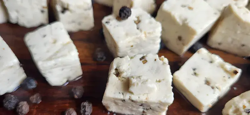 Cubes of PANEVO Black Pepper paneer on a dark wooden board, cracked peppercorns visible inside