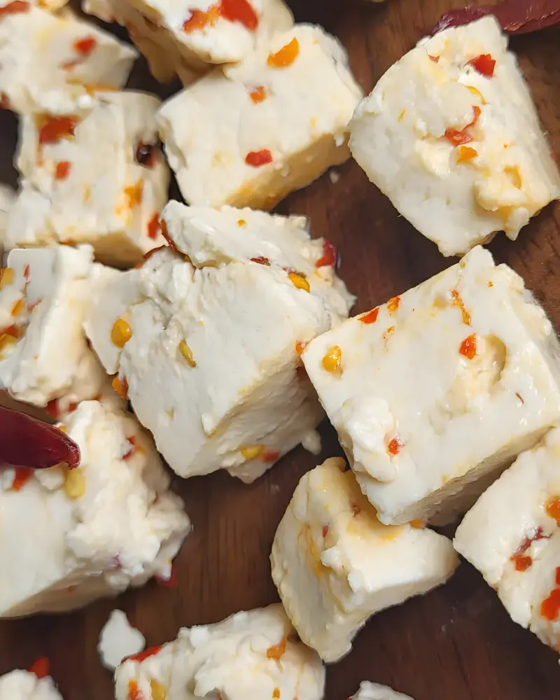 Cubes of PANEVO Red Chilli Flakes paneer on a wooden board, red chilli flakes set inside each piece