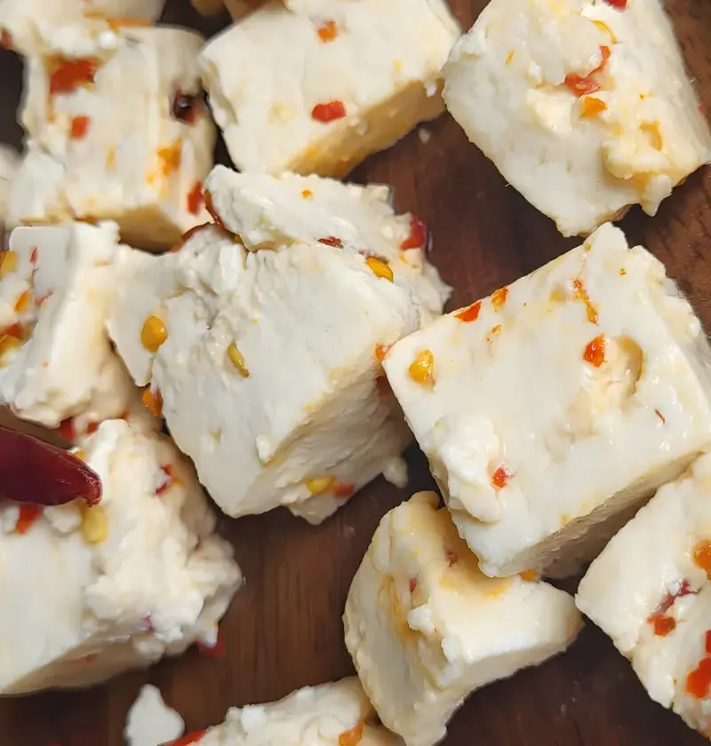 Cubes of PANEVO Red Chilli Flakes paneer on a wooden board, red chilli flakes set inside each piece